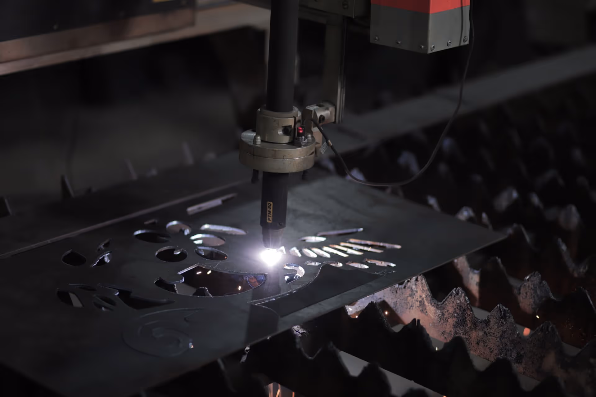 Primo piano della torcia plasma PTM-80 durante il taglio CNC di una lamiera — getto arancione e alone luminoso della camera di combustione